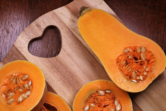 Butternut squash cut open on a wooden board, showing rich orange flesh and seeds inside.