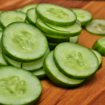 Spacemaster cucumber slices arranged on a wooden cutting board, showcasing the crisp, light green interior of this compact heirloom cucumber variety.