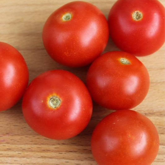 Close-up of ripe bright red Vilma micro dwarf cherry tomatoes displayed on a wooden table.